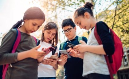 Four adolescents standing in a group, looking on their smart phones.